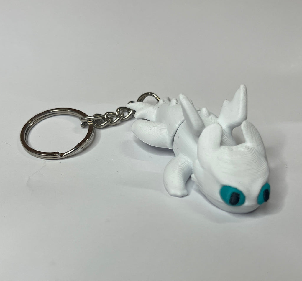 White dragon-shaped keychain with blue eyes on a light gray background