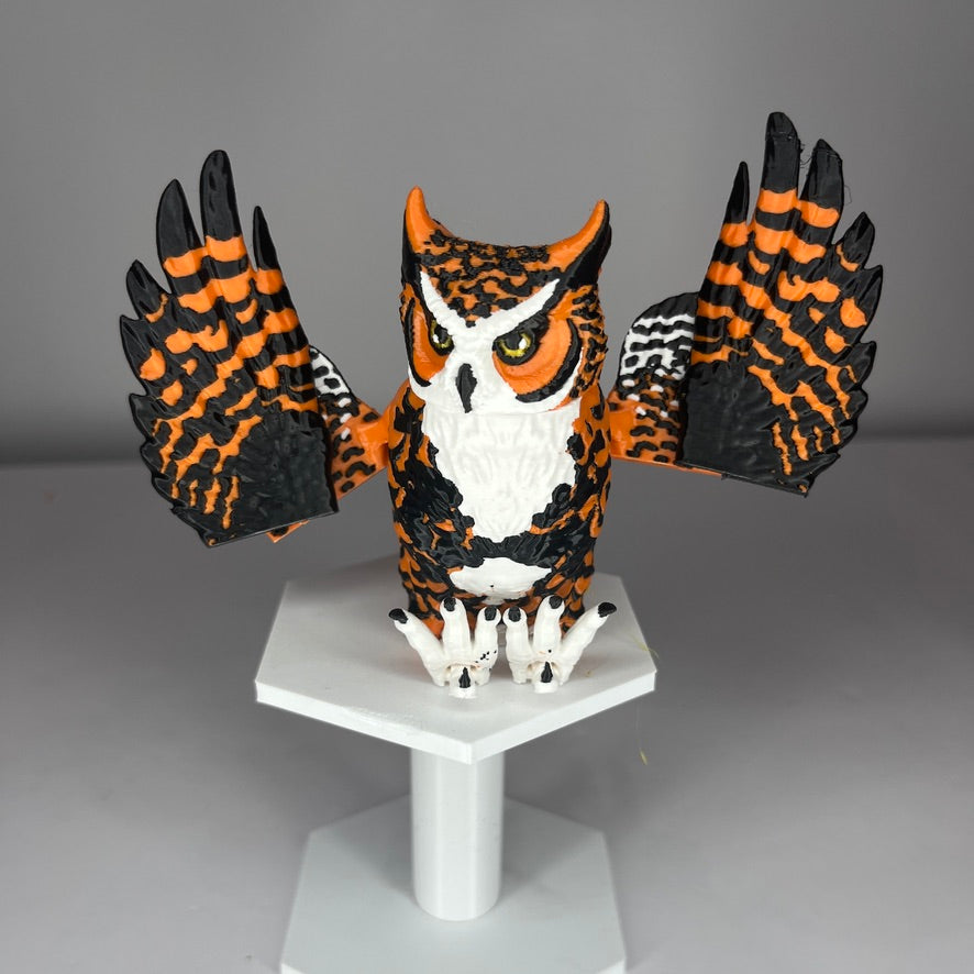 Model of an owl with orange, black, and white feathers on a gray background